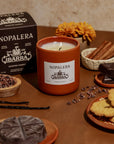 Nopalera Ibarra candle on a table with cookies, chocolate, and flowers
