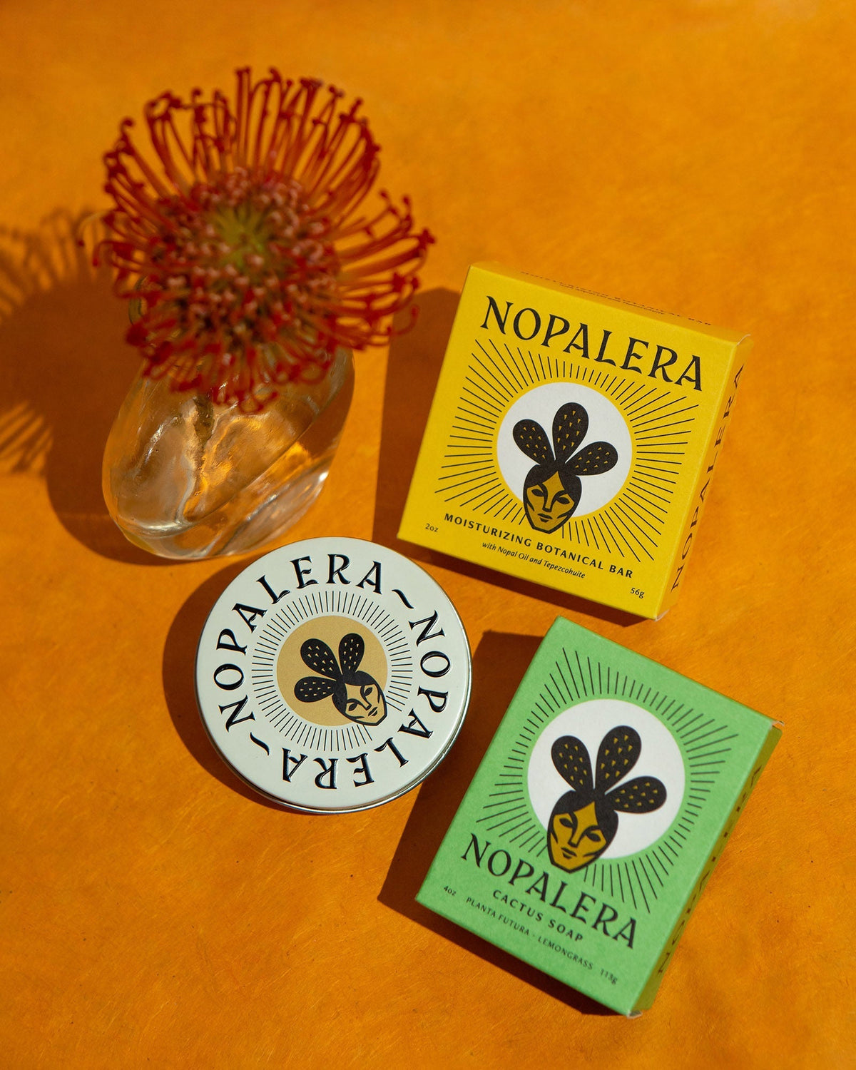 Nopalera Citrus Lotion Bar and Lemongrass Soap displayed with floral accents on a vibrant orange background.