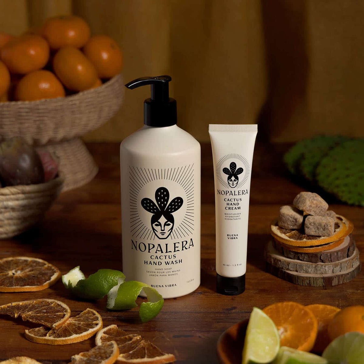 Nopalera Cactus Hand Wash  and hand cream with a large pump bottle and a smaller squeeze tube, styled on a wooden table with citrus fruits, dried orange slices, and green leaves in the background.