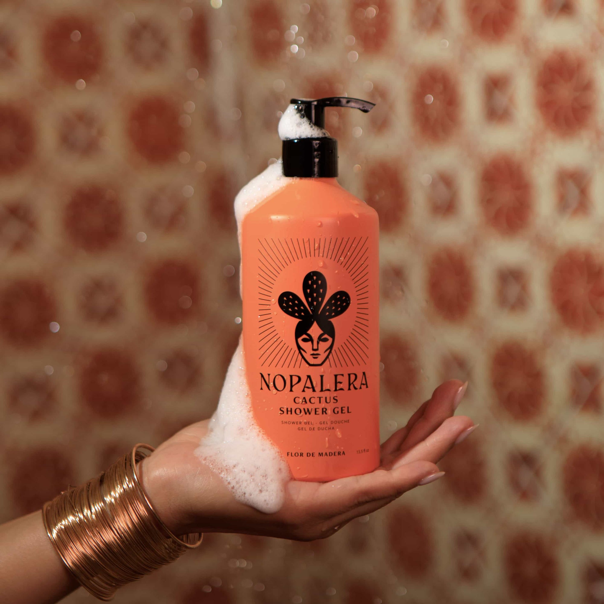 An orange pump bottle of Nopalera Cactus Shower Gel been hold by a hand in a  an orange background