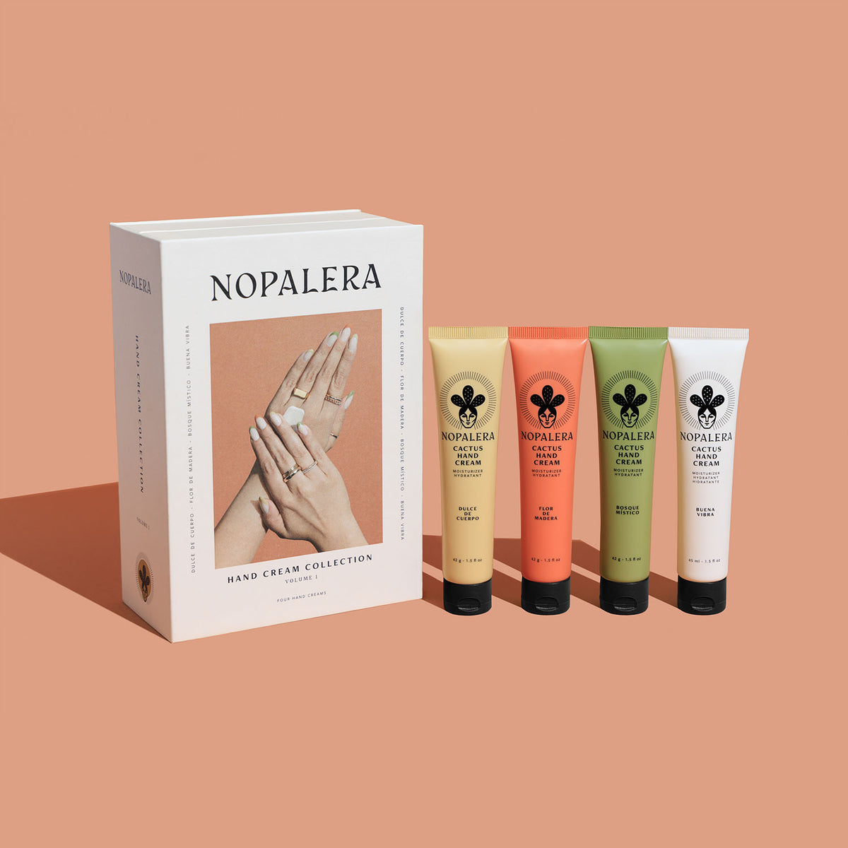 Nopalera Hand Cream Collection gift box with four Cactus Hand Cream tubes in Flor de Madera, Dulce de Cuerpo, Bosque Místico, and Buena Vibra scents, against a peach background.