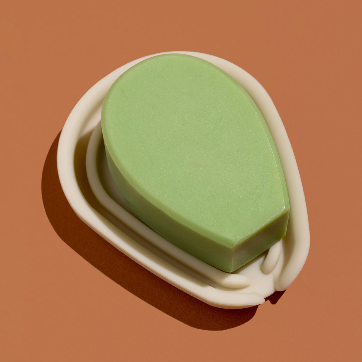 A green cactus-shaped bar of soap resting in a white silicone soap dish against a brown background.