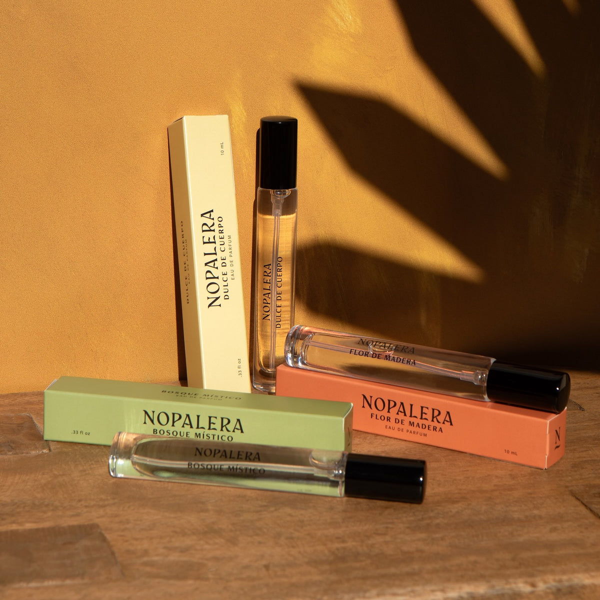 Nopalera travel perfume rollers in Dulce de Cuerpo, Flor de Madera, and Bosque Místico fragrances displayed with their boxes on a warm background