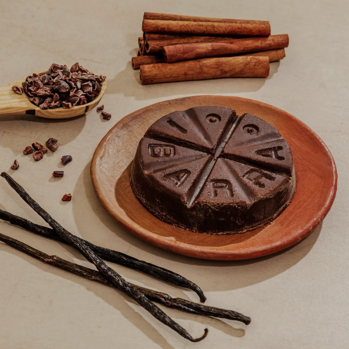 Chocolate cake with 'Fudgy' branding on a plate, surrounded by vanilla beans, cinnamon sticks, and cacao nibs.