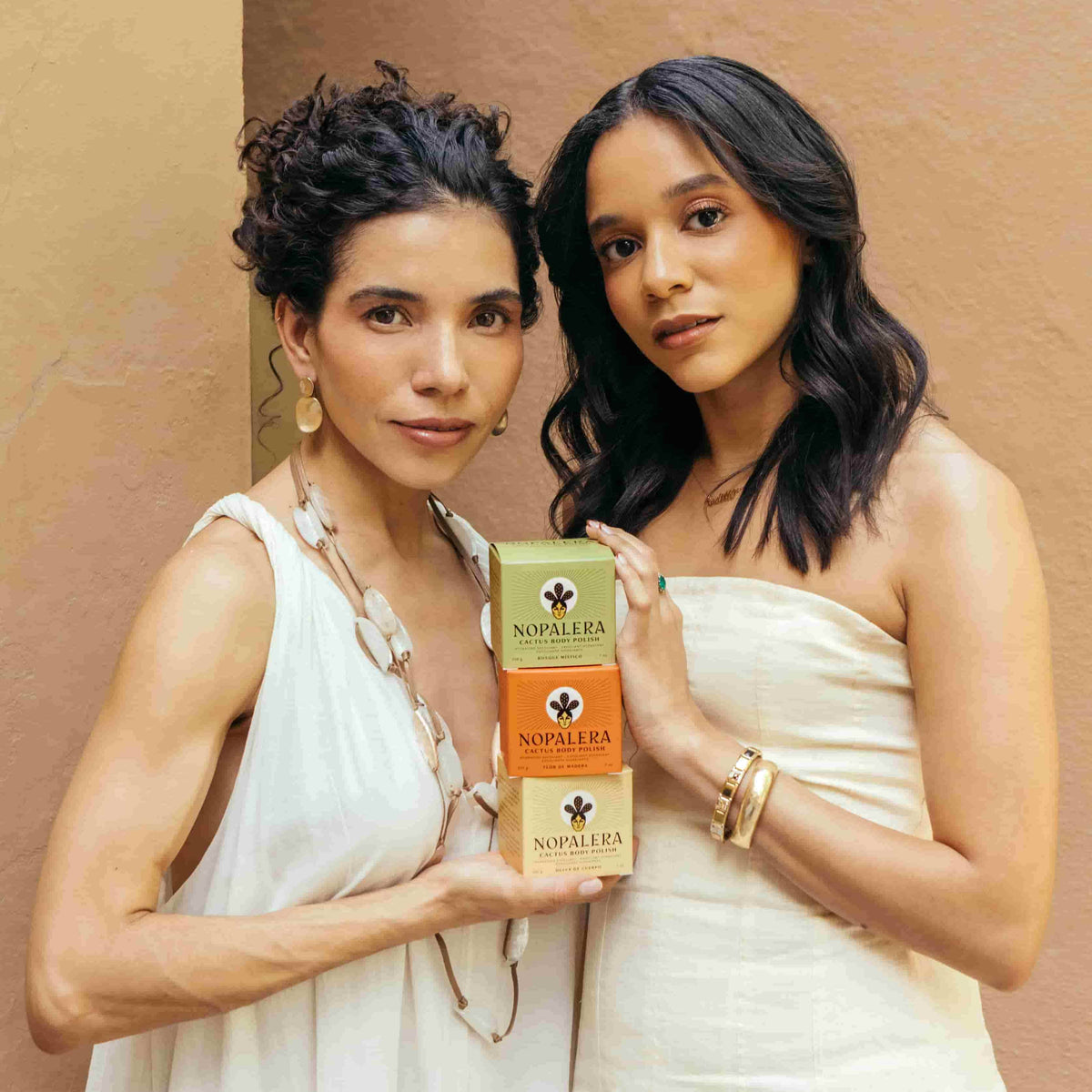 Two women holding Nopalera body polishes against a beige background
