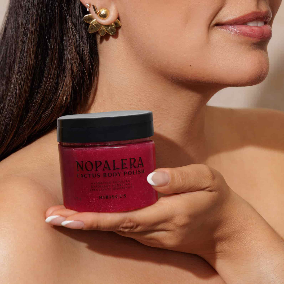 Woman holding a jar of Nopalera body polish hibiscus  against a neutral background