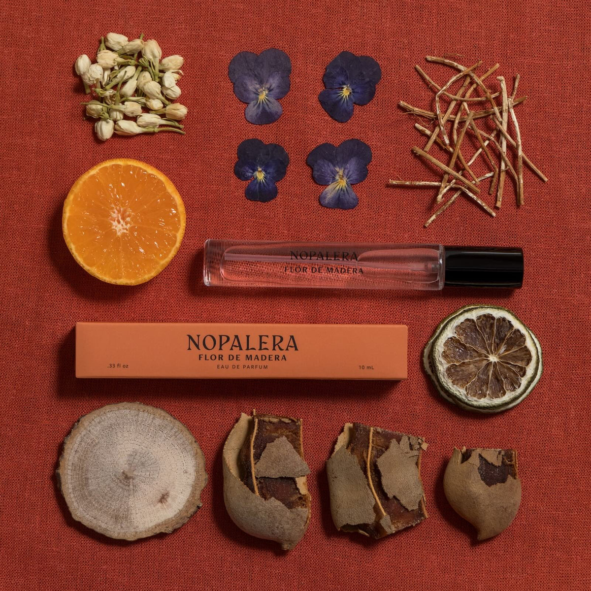 Nopalera Luxury Mexican fragrance Flor de Madera travel perfume roller surrounded by fragrance ingredients like orange, dried citrus, flowers, herbs, and wood notes
